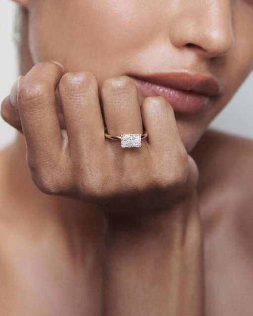 Female model wearing a custom 1.1 carat east-west radiant cut lab diamond engagement ring in 14K gold, emphasizing the extensive horizontal finger coverage and modern minimalist aesthetic of the design.