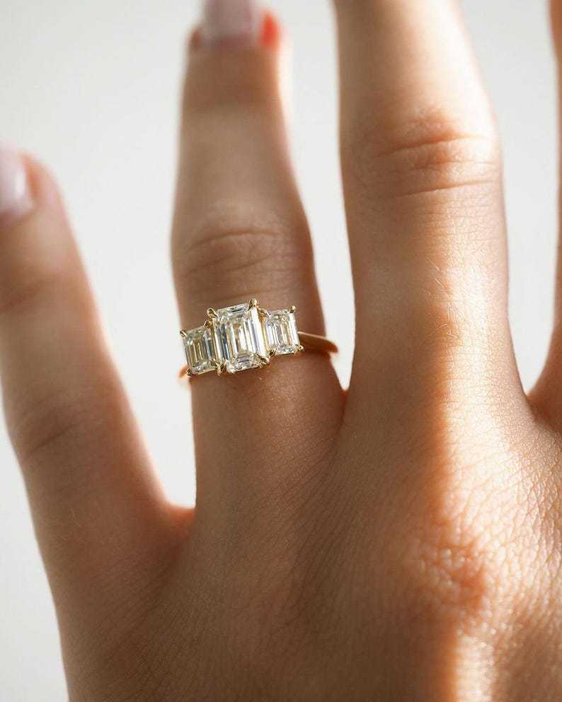 A bespoke 2.75 carat emerald cut lab-grown diamond three-stone ring worn on a finger, demonstrating scale, finger coverage, and face-up dimensions.