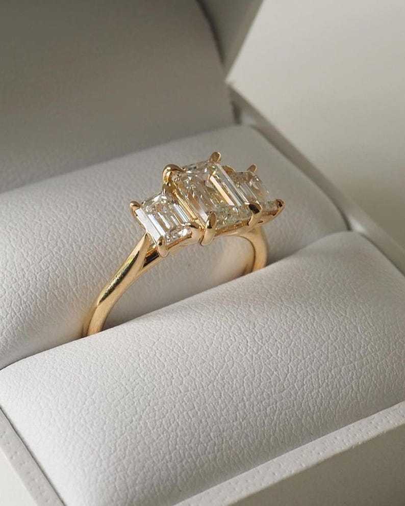 Close-up inside a white presentation box highlighting the E-F color VVS-VS clarity emerald cut lab-grown side diamonds and 14K gold band.