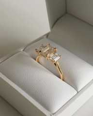 A 14K gold three-stone emerald cut lab-grown diamond engagement ring elegantly displayed inside a white luxury presentation box.