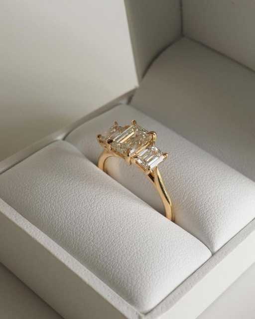 A 14K gold three-stone emerald cut lab-grown diamond engagement ring elegantly displayed inside a white luxury presentation box.