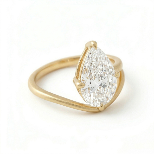 Angled top-down view of a stunning 3 carat pear cut lab grown diamond ring, highlighting the exceptional E color and asymmetrical 14K matte gold bypass design.