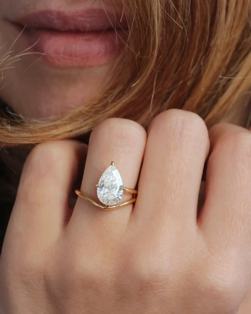 Lifestyle shot of a woman touching her hair while wearing a gorgeous 3 carat pear shaped lab diamond engagement ring with a 14K yellow gold bypass band.