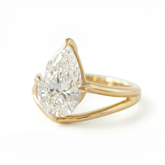 Macro profile close-up of a flawless VVS2 E color 3 carat pear lab created diamond secured by asymmetrical claw prongs on a 14K yellow gold brushed band.