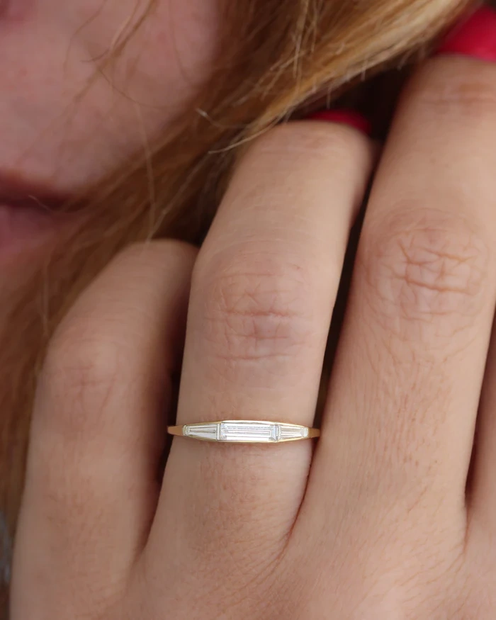 Close up of a woman hand with red nail polish wearing a 14K gold bezel set tapered baguette lab diamond ring.