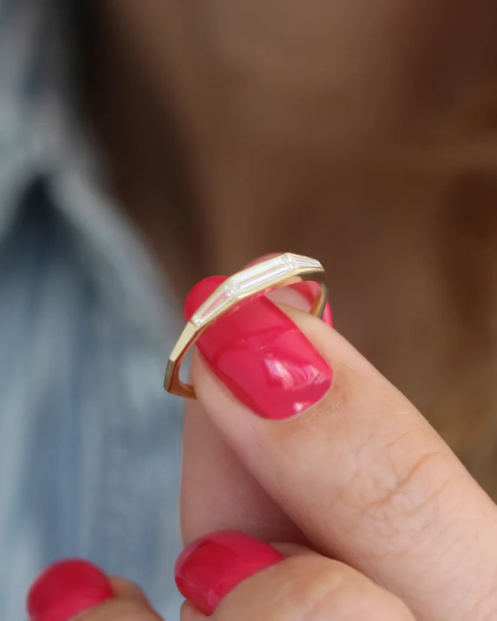 Fingers holding a 14K gold bezel set baguette lab diamond ring highlighting the smooth low profile setting.