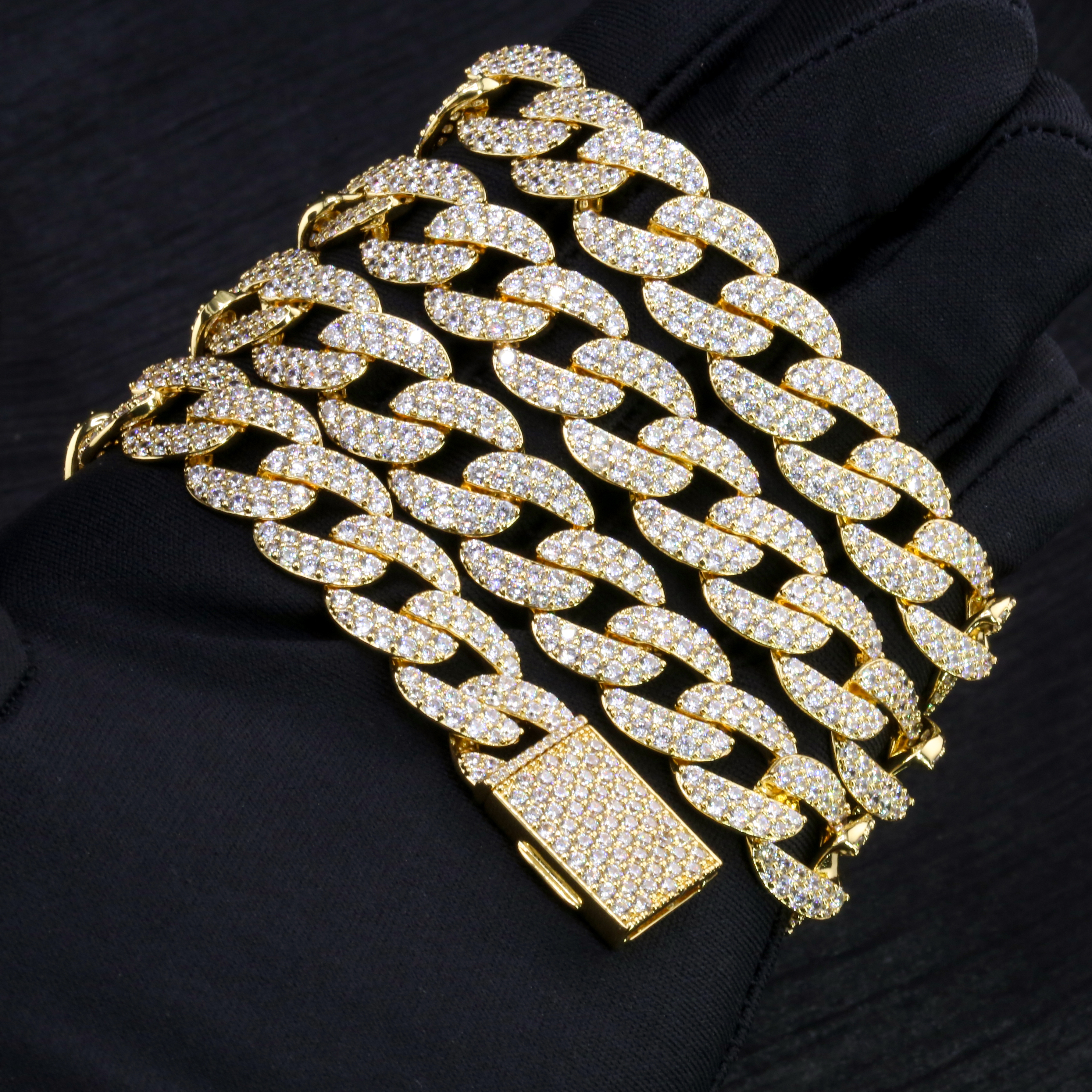 Close-up of a folded 13mm iced out moissanite Cuban link bracelet in gold-plated S925 silver resting on a black glove, showcasing the VVS clarity micro-pave stones and a secure diamond box clasp.