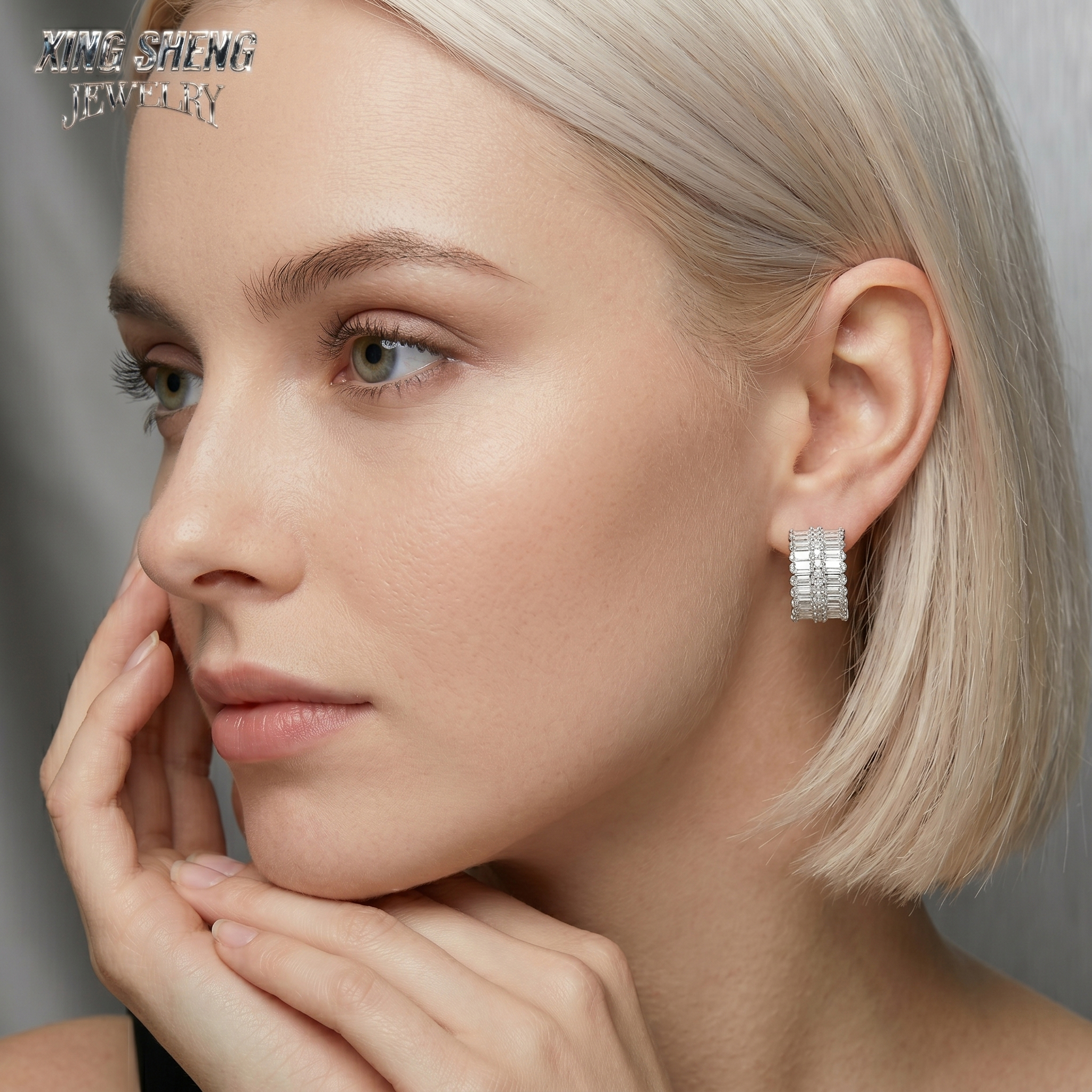 Elegant blonde model wearing Xing Sheng Jewelry custom moissanite hoop earrings, looking to the side against a sleek grey background.