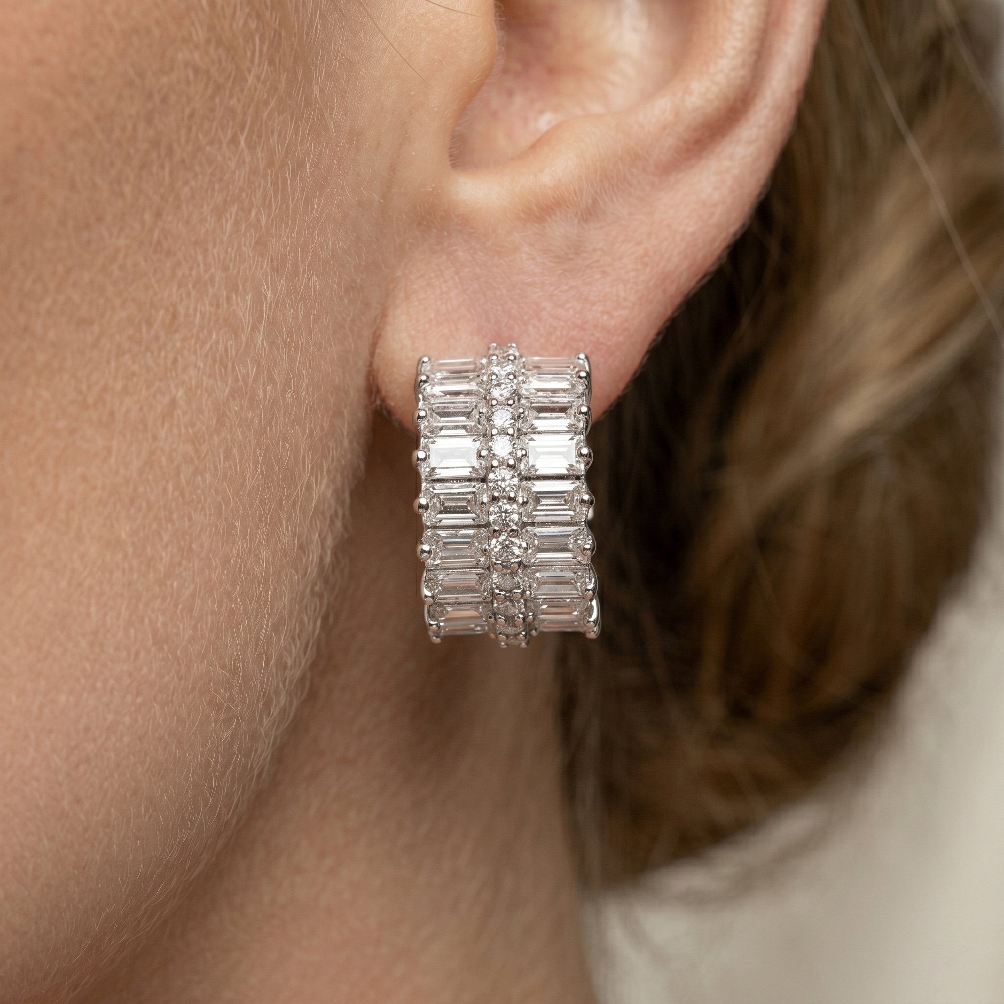Close-up of a woman wearing thick baguette and round cut moissanite huggie earrings, showing the perfect fit and sparkle on the earlobe.