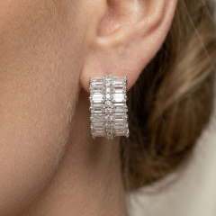 Close-up of a woman wearing thick baguette and round cut moissanite huggie earrings, showing the perfect fit and sparkle on the earlobe.