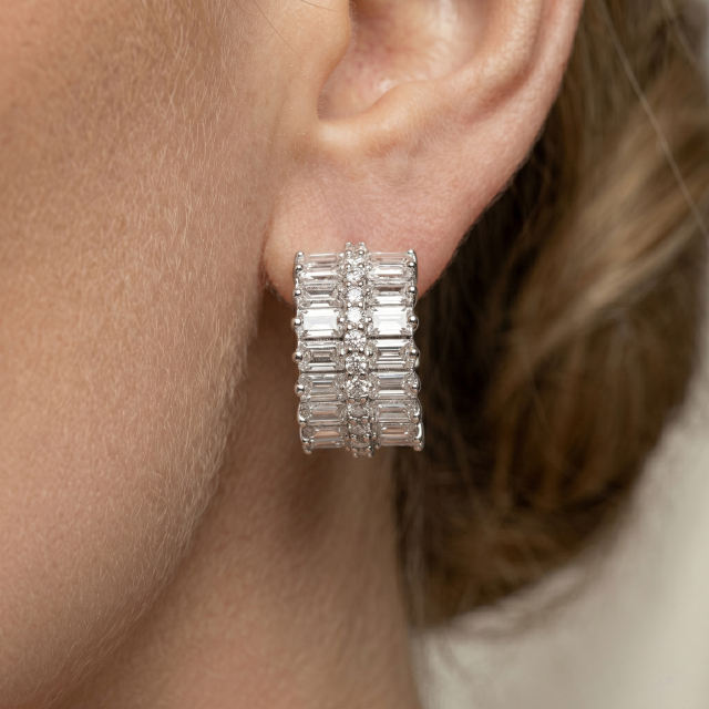 Close-up of a woman wearing thick baguette and round cut moissanite huggie earrings, showing the perfect fit and sparkle on the earlobe.