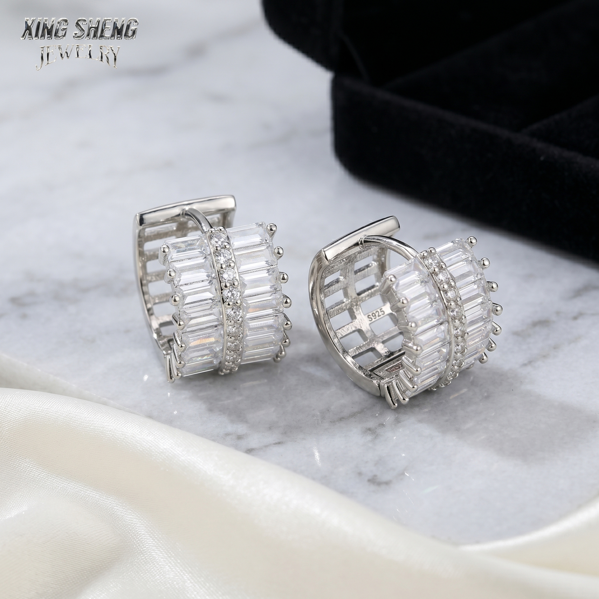 Detailed view of the S925 stamp inside moissanite hoop earrings resting on white marble, with a black fine jewelry presentation box in the background.