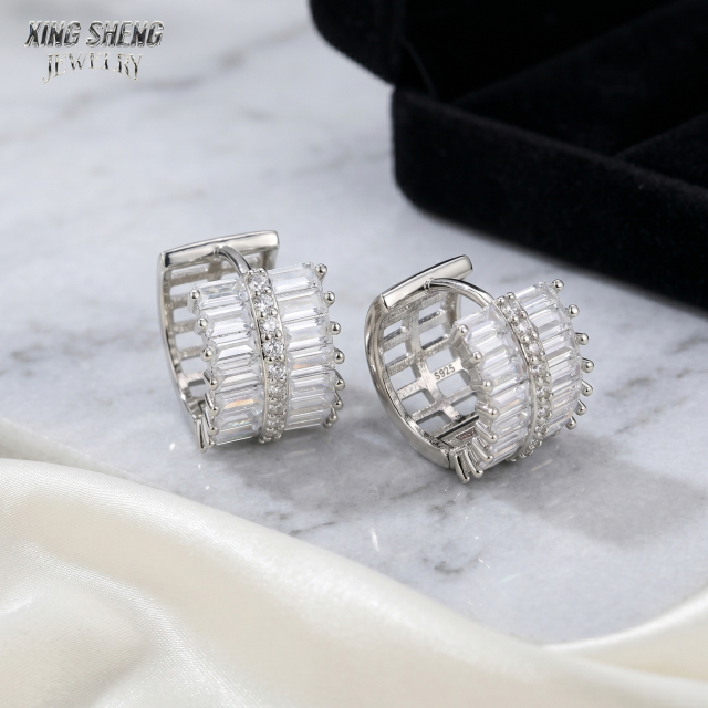 Detailed view of the S925 stamp inside moissanite hoop earrings resting on white marble, with a black fine jewelry presentation box in the background.