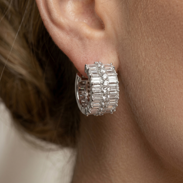 Side profile close-up of a woman's ear wearing flawless VVS baguette and round cut moissanite silver earrings, highlighting the Excellent cut fire.