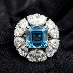 Top-down flat lay view on black texture emphasizing the geometric perfection of the Asscher cut blue topaz center and the brilliant crushed-ice fire of the pear moissanite halo.
