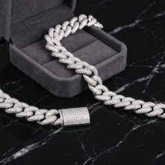 A premium 16mm iced-out moissanite Cuban link chain crafted in S925 sterling silver, draped elegantly from a grey velvet jewelry box onto a black marble surface, highlighting its brilliant diamond-like fire and secure box clasp.