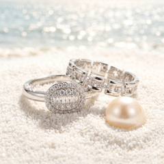 S925 sterling silver moissanite wedding band and engagement ring set displayed on white beach sand next to a pearl.