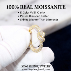 Close up of a gloved hand holding a brilliant D color VVS1 moissanite love knot earring that passes diamond testers and shines brighter than diamonds.