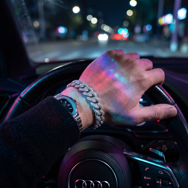 Close-up of a 10MM Moissanite Cuban Link Chain bracelet on a driver's wrist, showcasing extreme rainbow fire and brilliance under night lights.