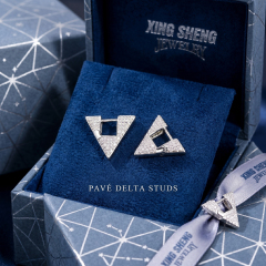 The Pavé Delta Studs resting elegantly on textured blue velvet inside a premium geometric-patterned presentation box tied with a branded silver ribbon, ideal for luxury gifting.