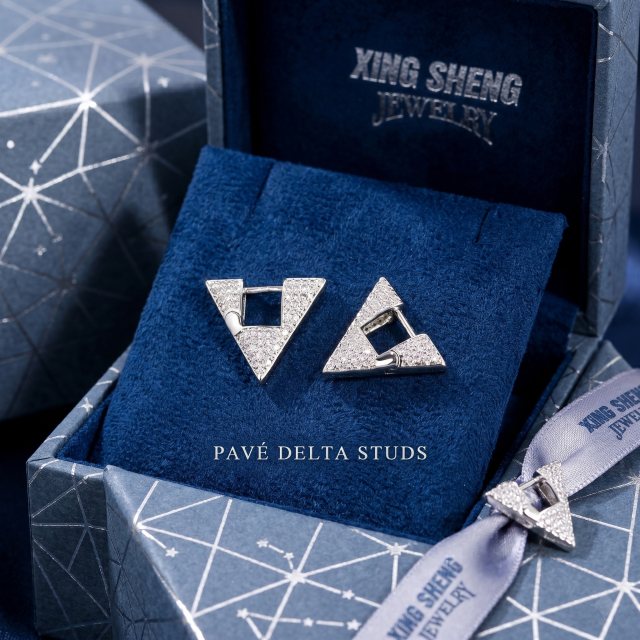 The Pavé Delta Studs resting elegantly on textured blue velvet inside a premium geometric-patterned presentation box tied with a branded silver ribbon, ideal for luxury gifting.