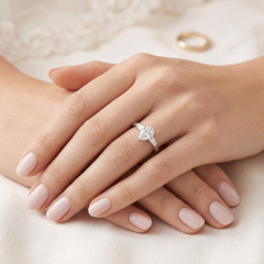 A woman's hands resting on white fabric, wearing a brilliant 18K white gold engagement ring with a teardrop lab-grown diamond.