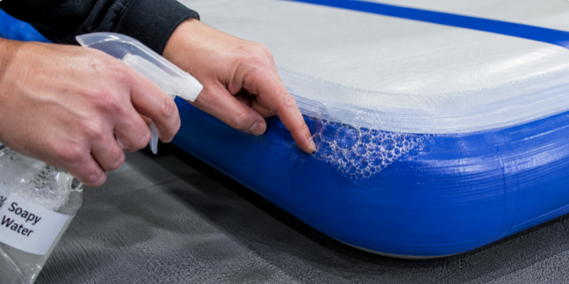 Close-up of a soapy water bubble leak test being performed on the seam of an inflated air track mat