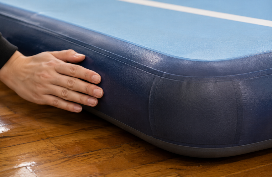 `Macro view of a heat-welded seam and reinforced corner on an inflatable air track, showing multi-layer bonding and a rounded edge`