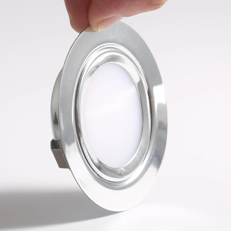 Hand holding a slim recessed LED downlight with a polished stainless steel rim