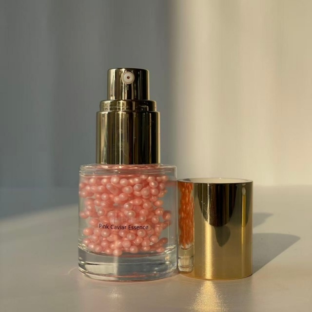 Wholesale Pink Caviar Essence display—transparent glass bottle with golden press pump & cap, holding pink beaded essence, ideal for B2B skincare sourcing & private label customization