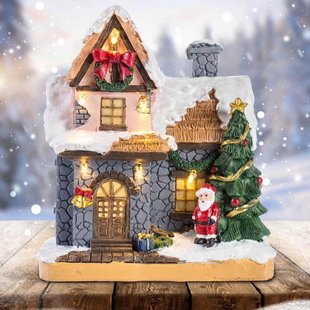 Wholesale innodept12 LED lighted Christmas village house with Santa Claus, snow-covered roof, and festive tree on a wooden tabletop.