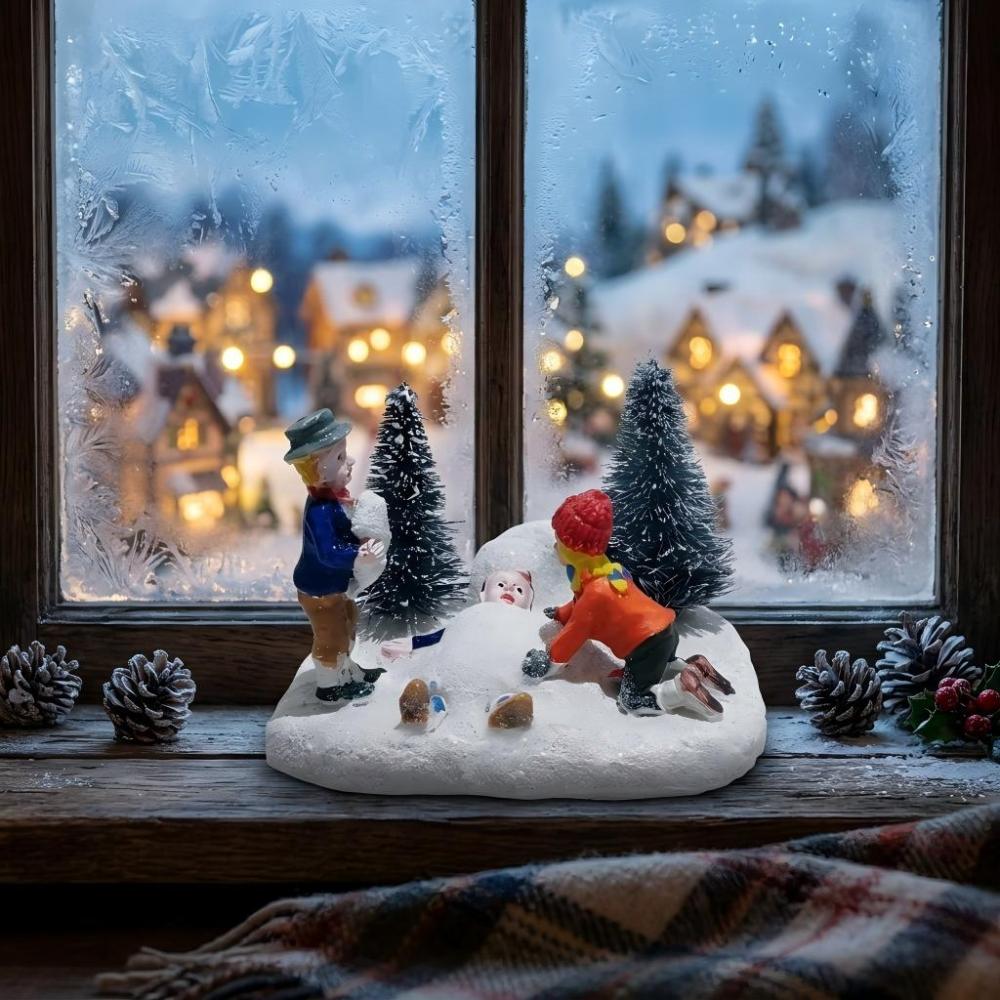 Christmas village children building snowman figurine on a rustic wooden windowsill with a blurry snowy village background.