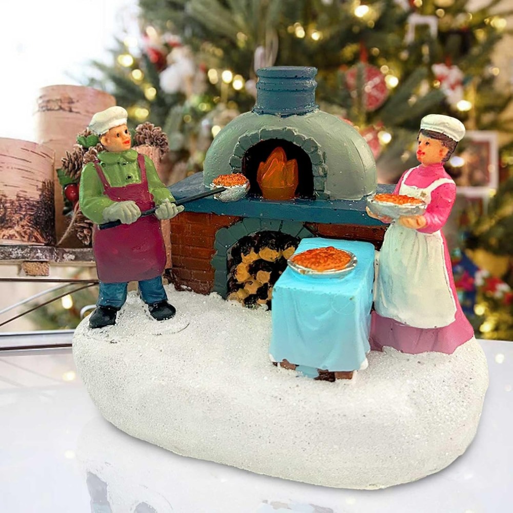 Hand-painted Christmas village scene featuring two baker figurines, a glowing stone pizza oven, and a snow-covered base for festive wholesale decor.