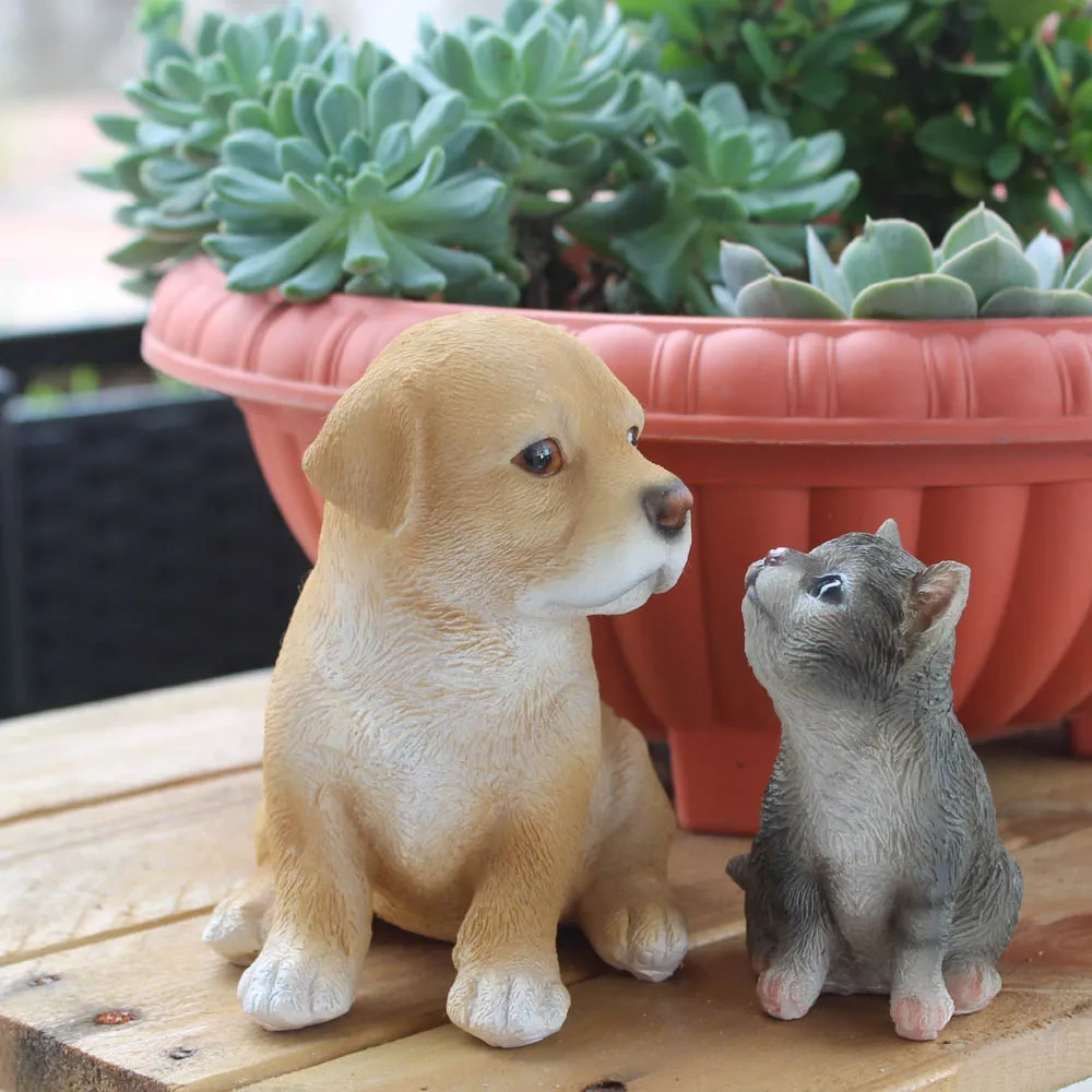 Cute resin golden puppy and grey kitten figurines sitting together on a wooden table next to a succulent flower pot