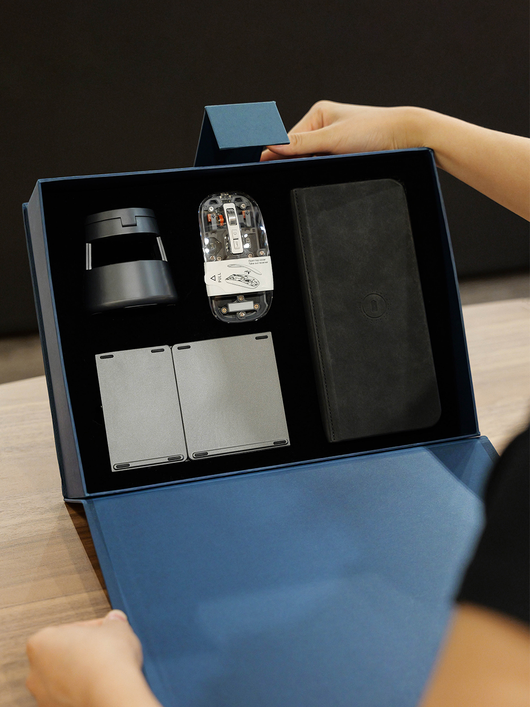 Blue gift box with a transparent mouse, folded silver keyboard, black folding item and compact dark accessory