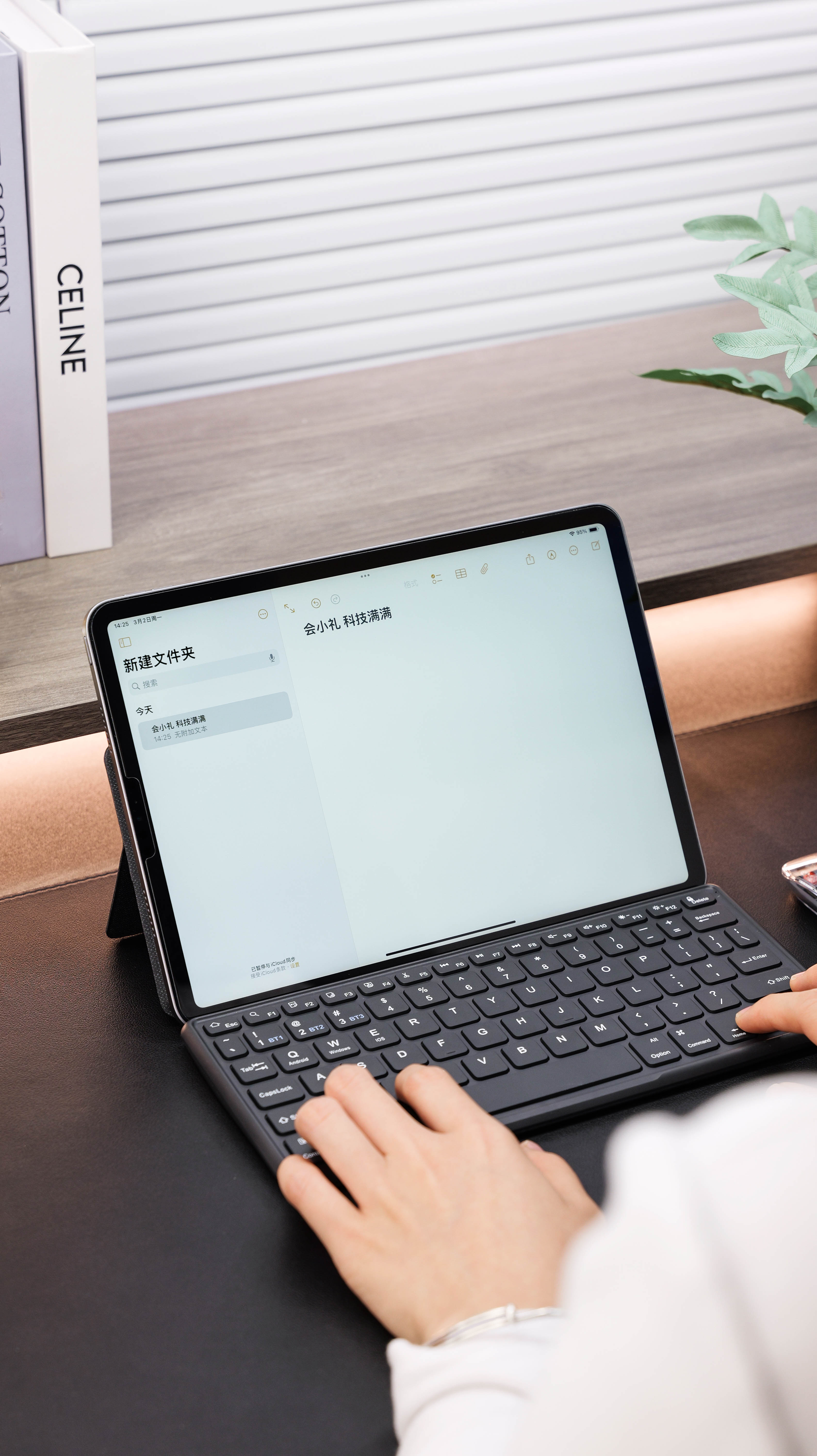 Hands typing on a compact keyboard in front of a tablet displaying a demonstration note