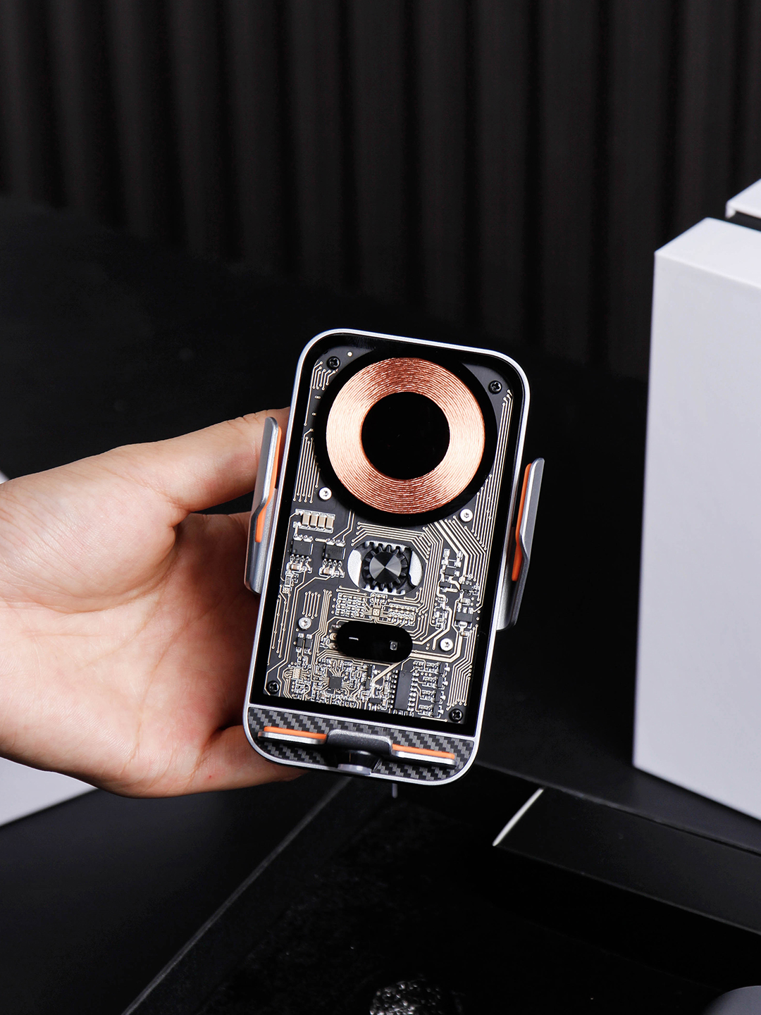 Hand holding a transparent-front phone holder with a visible copper-colored coil and side grips
