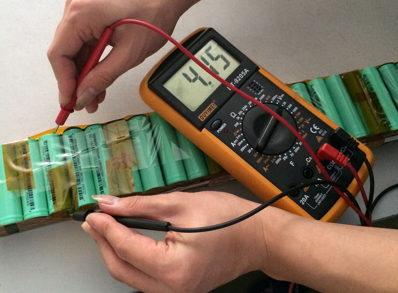 A technician using a digital multimeter to measure the output voltage of an e-bike battery charger