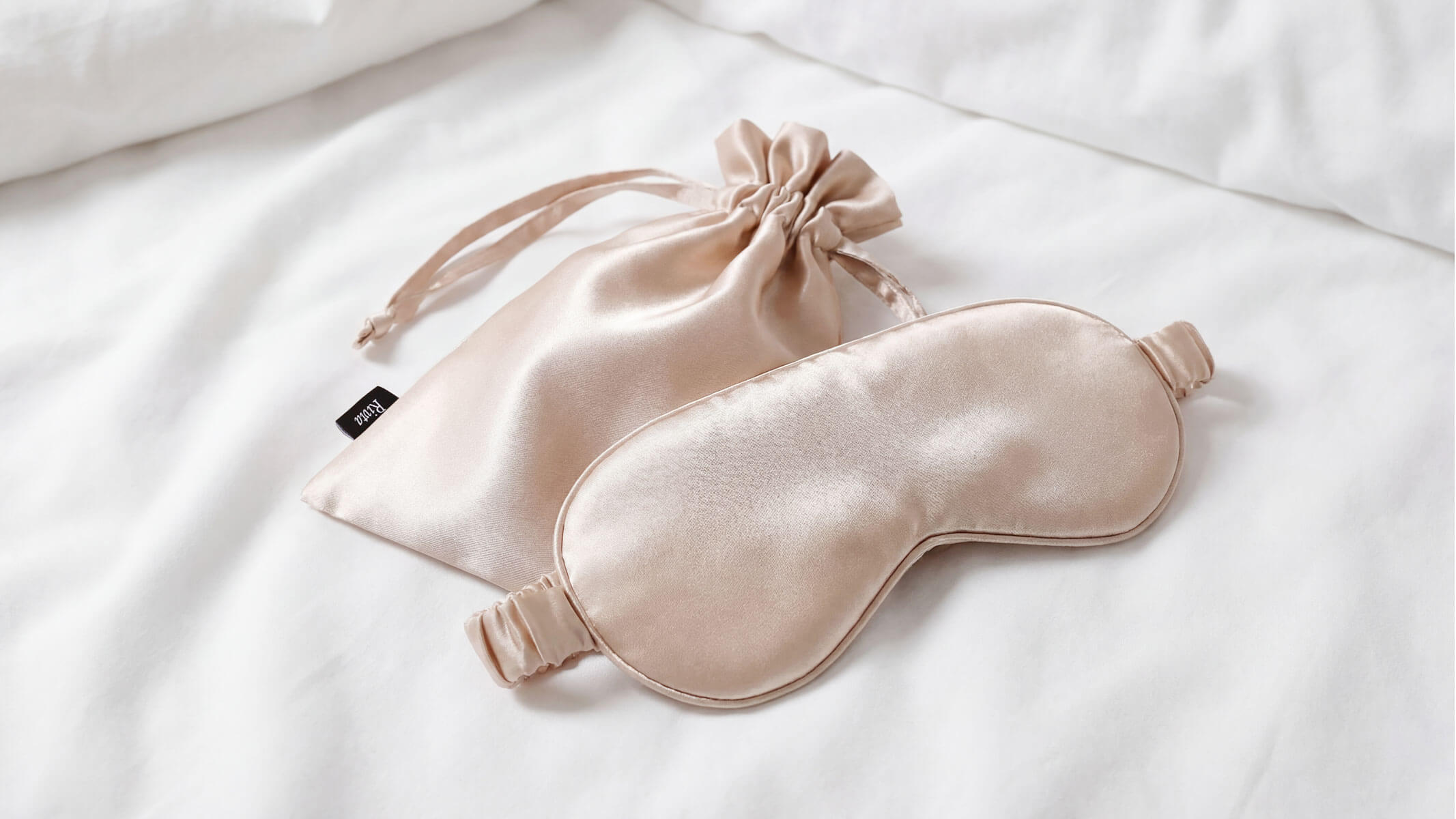 A close-up shot of a luxurious, silky sleep mask made from recycled RPET satin, resting on clean white bedding.