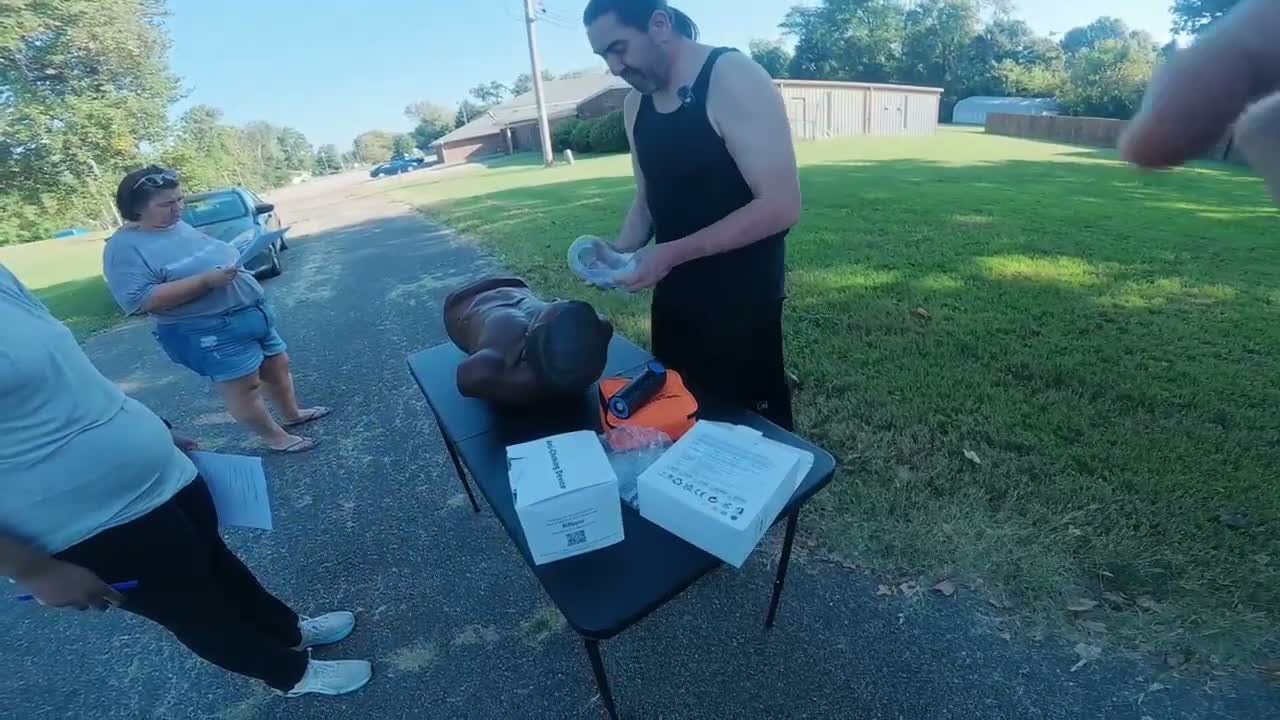 Participant holding a mask beside an adult training manikin and printed materials