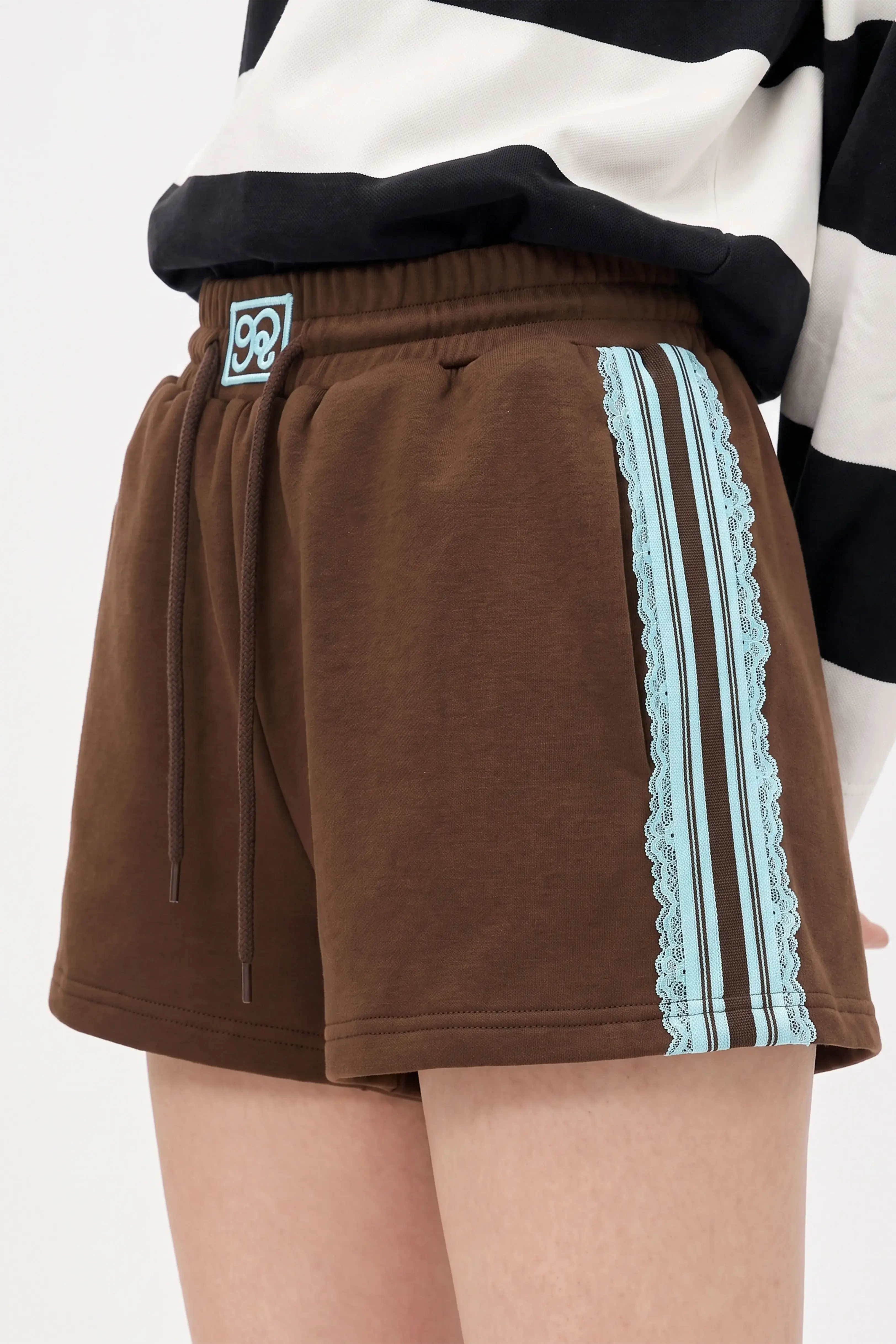 Close-up view of brown cotton sweat shorts with delicate side lace trim detail