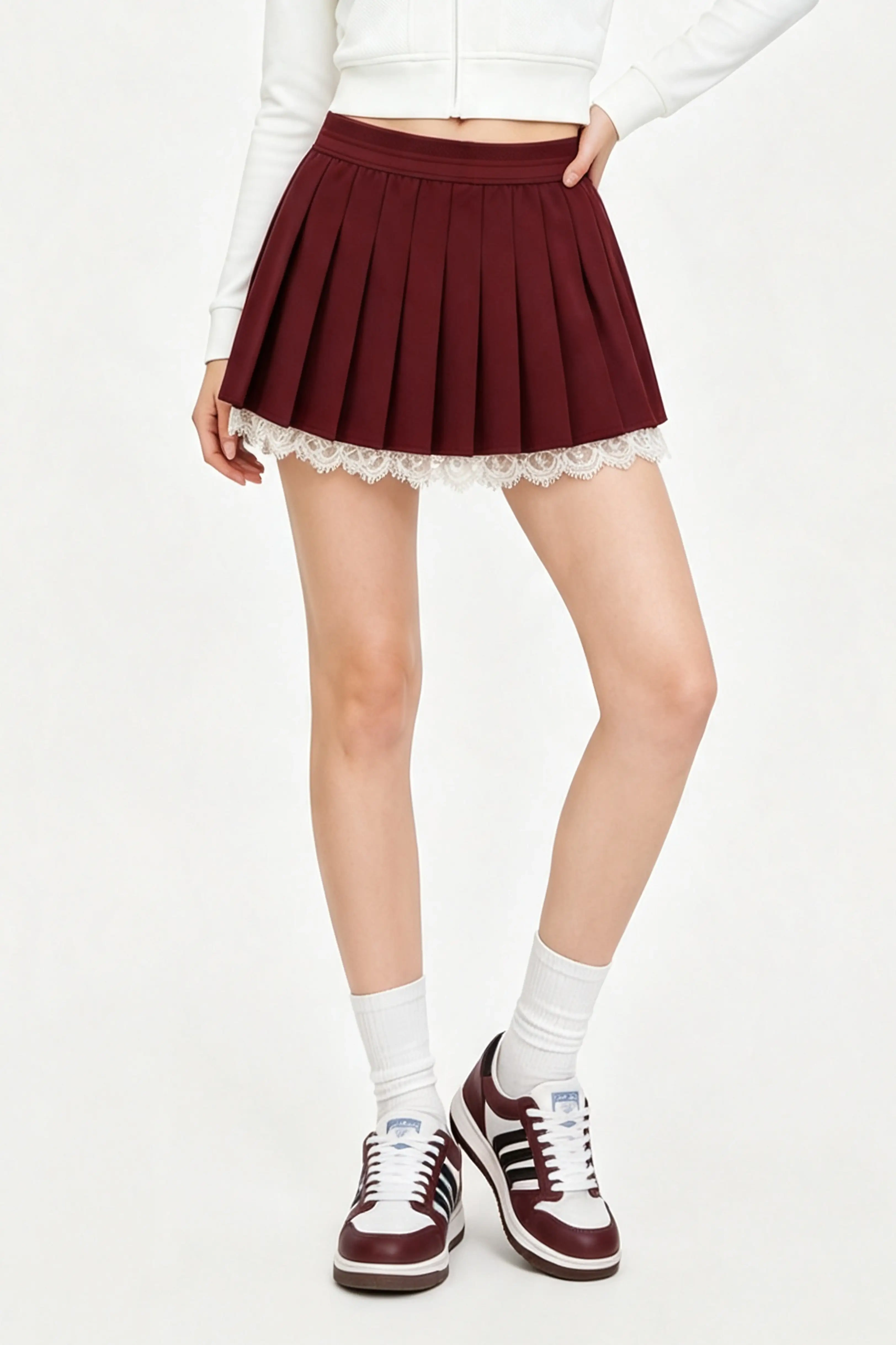 Front view of a woman wearing a high waisted burgundy tennis skirt with floral lace edging and sneakers.