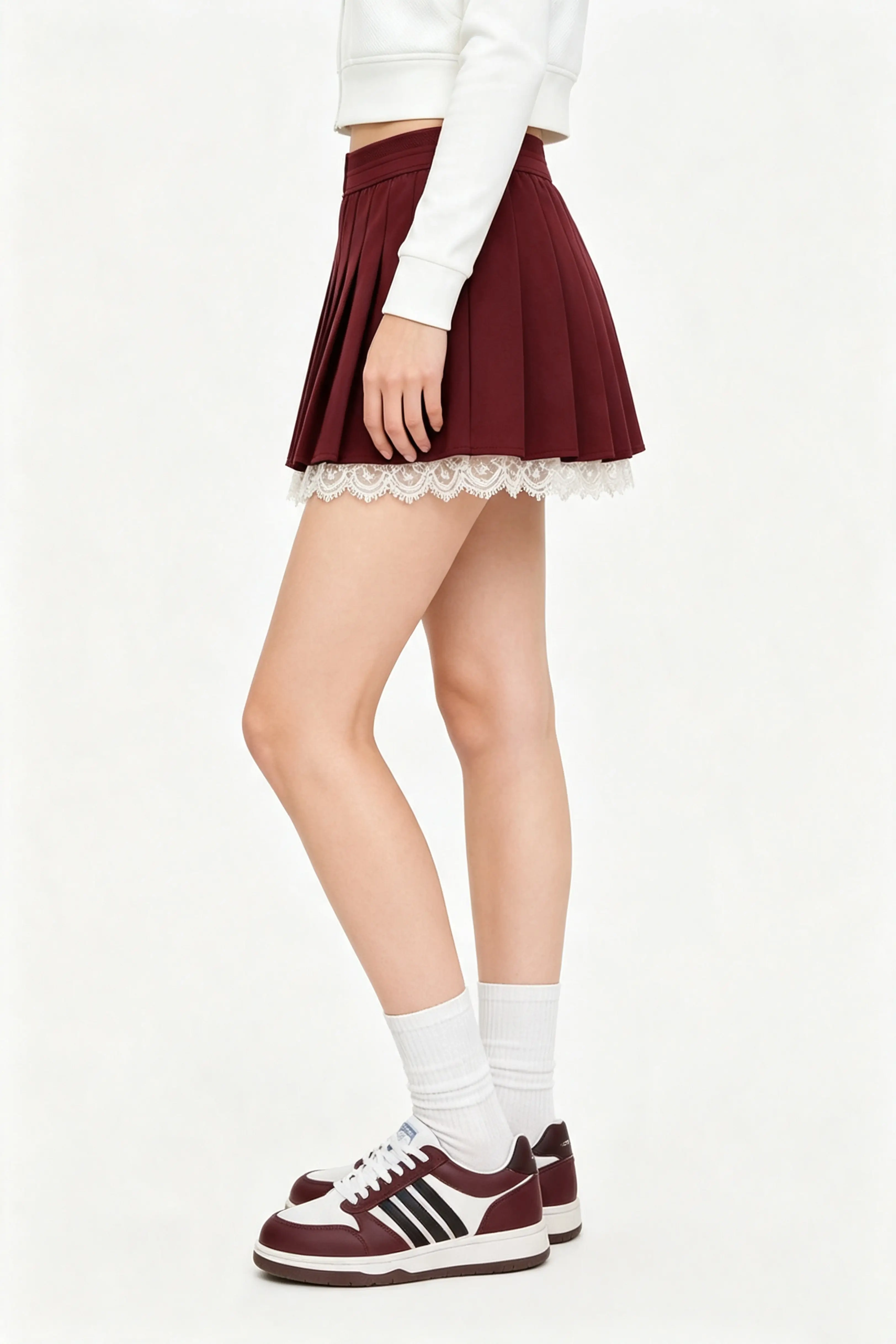 Side profile shot of a high waisted burgundy tennis skirt featuring a pleated flared style and delicate lace accent.