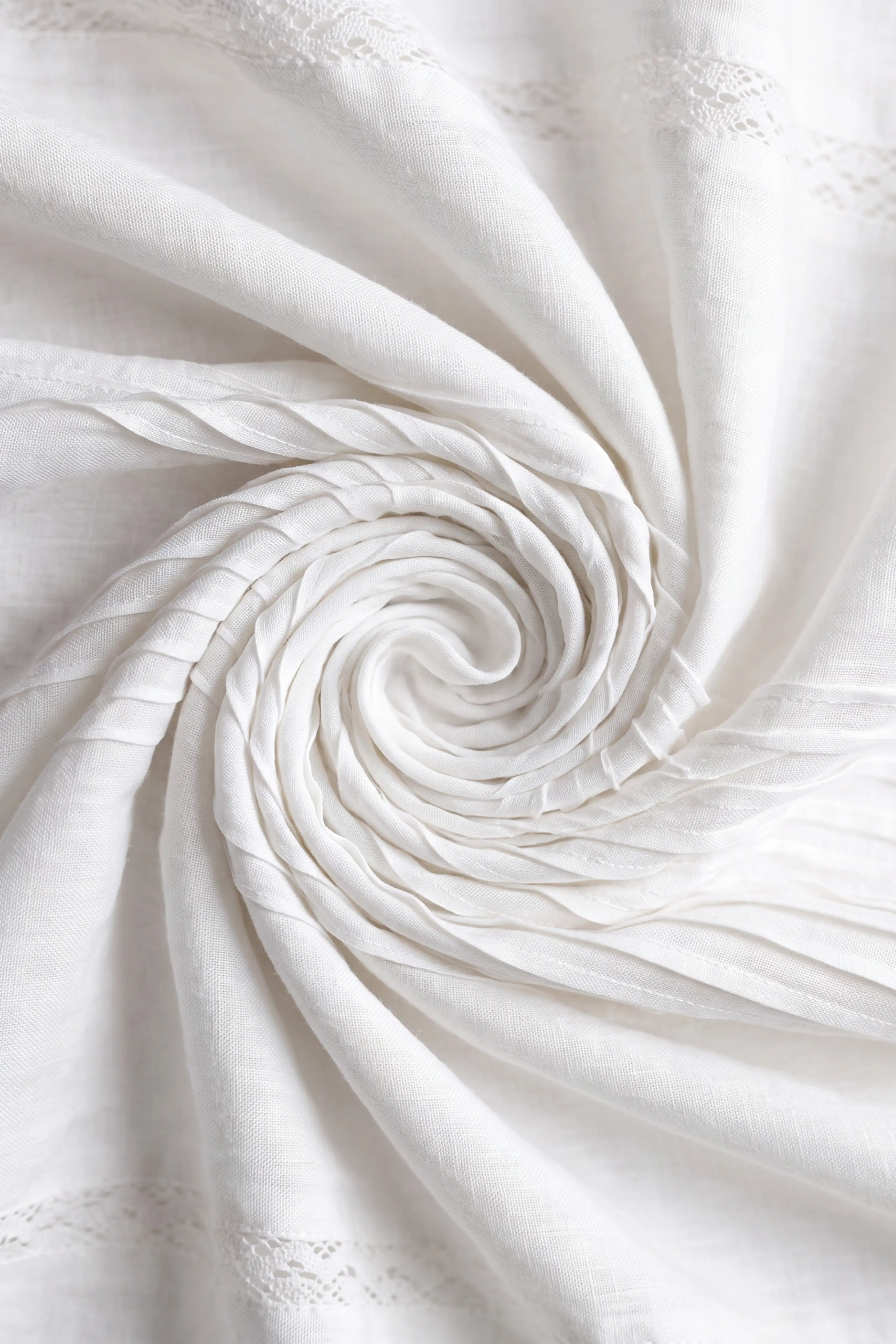 Extreme close-up shot highlighting the swirled texture, fine pleats, and woven fabric quality of the white midi skirt.