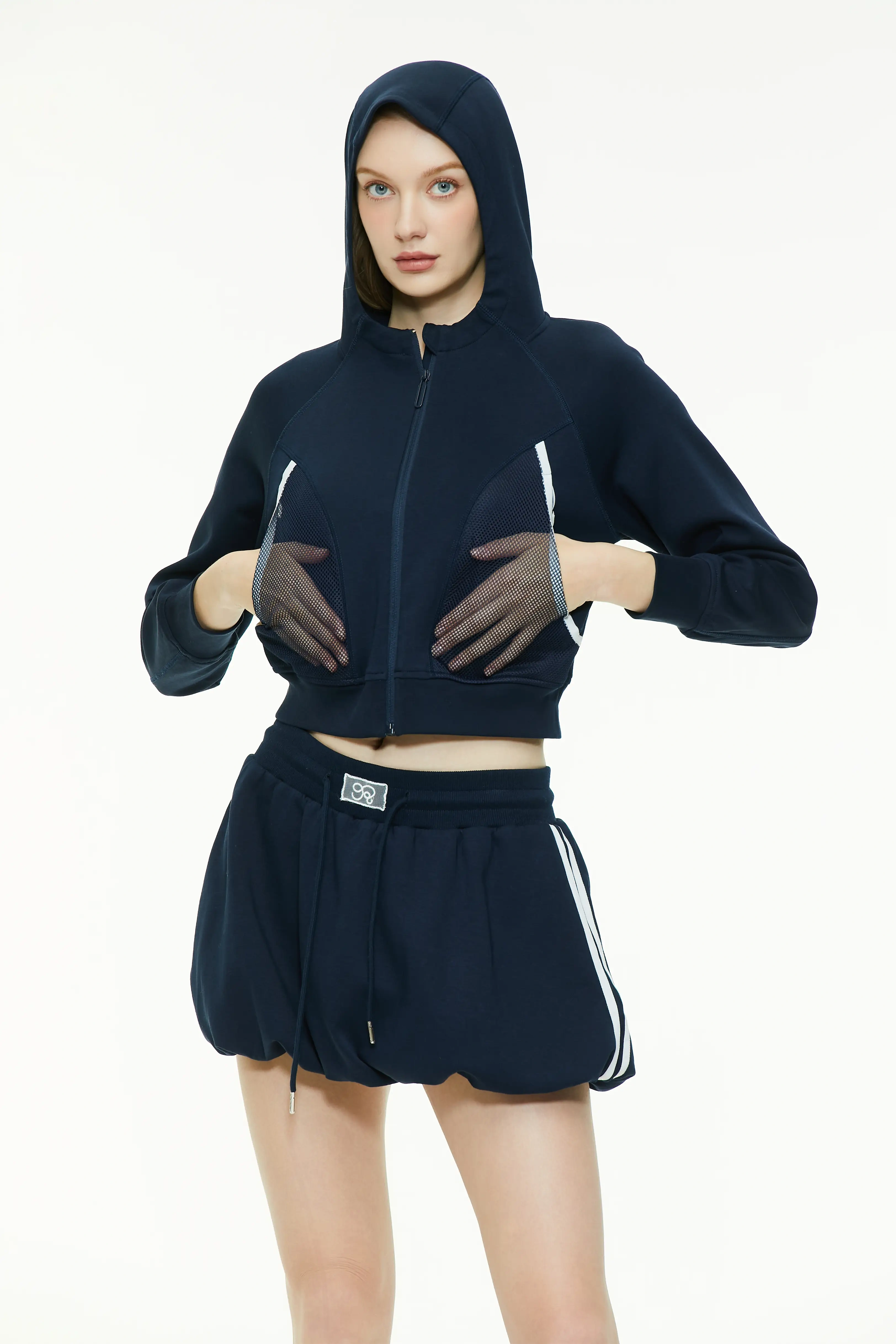 Front view of a model wearing a navy blue cropped zip-up hoodie with the hood pulled up over her head.