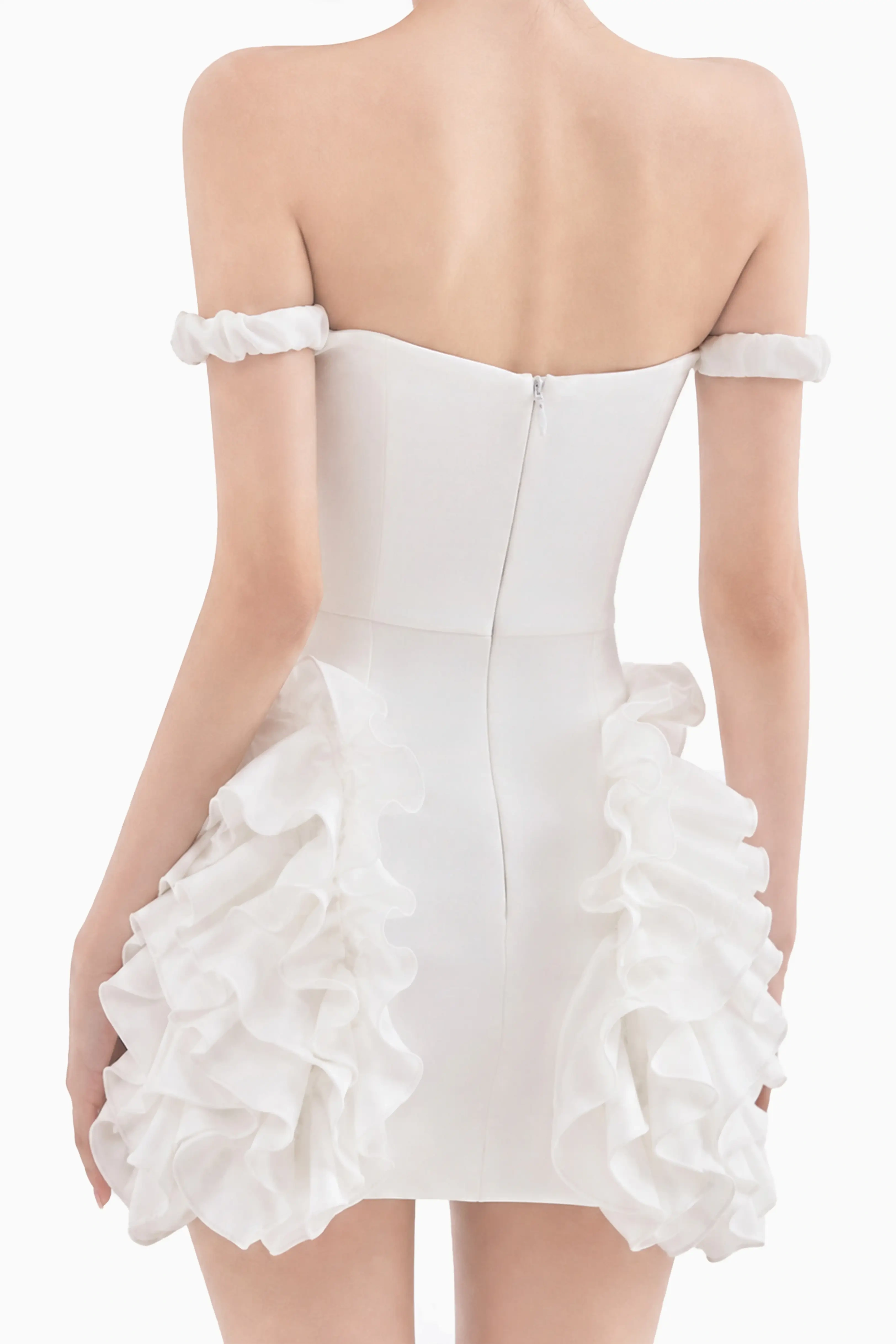 Back view of a model in a white ruffle mini dress featuring an off-the-shoulder design, back zipper closure, and side ruffles.