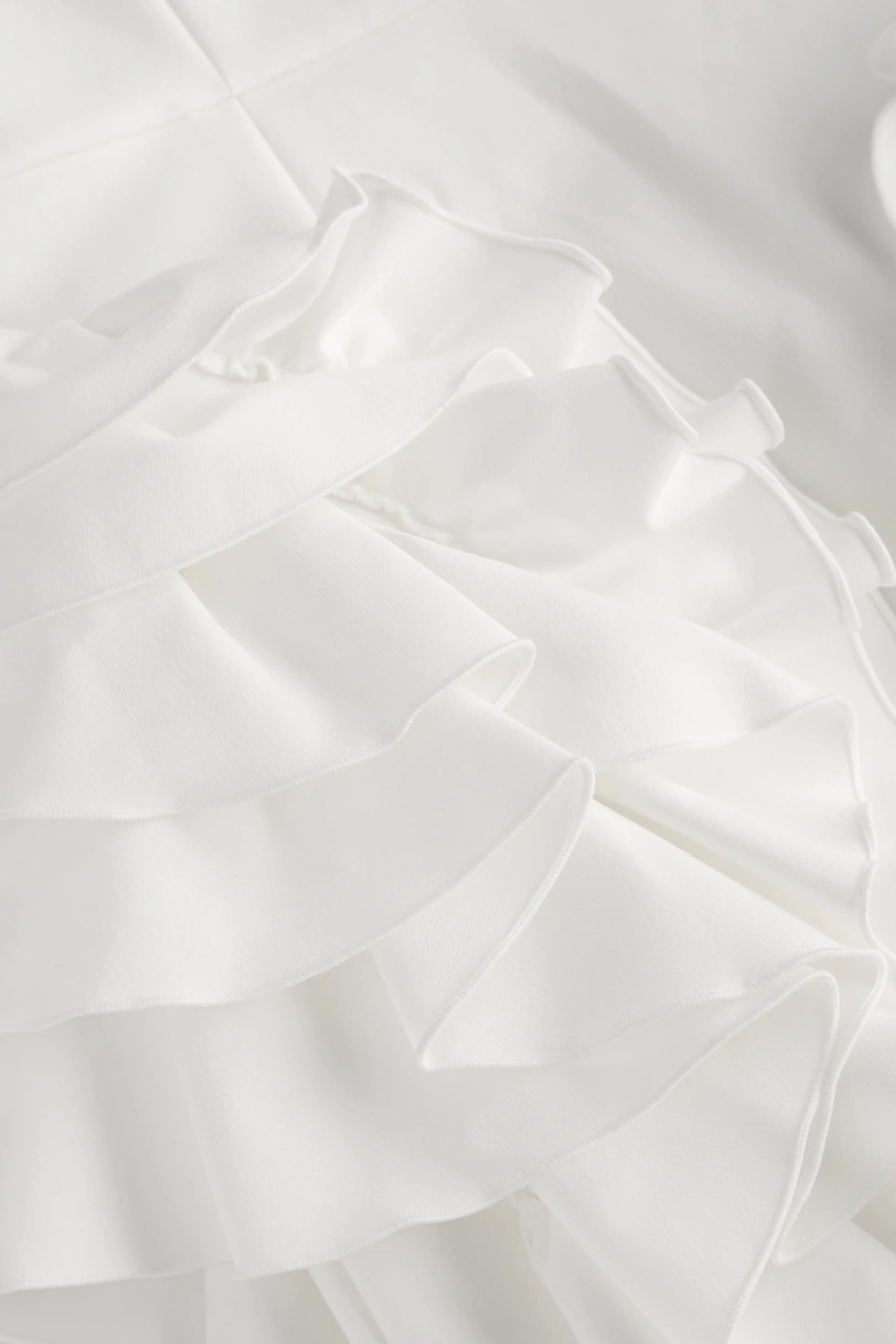 Extreme close-up view highlighting the fine pleated fabric texture and delicate ruffle details of the white mini dress.