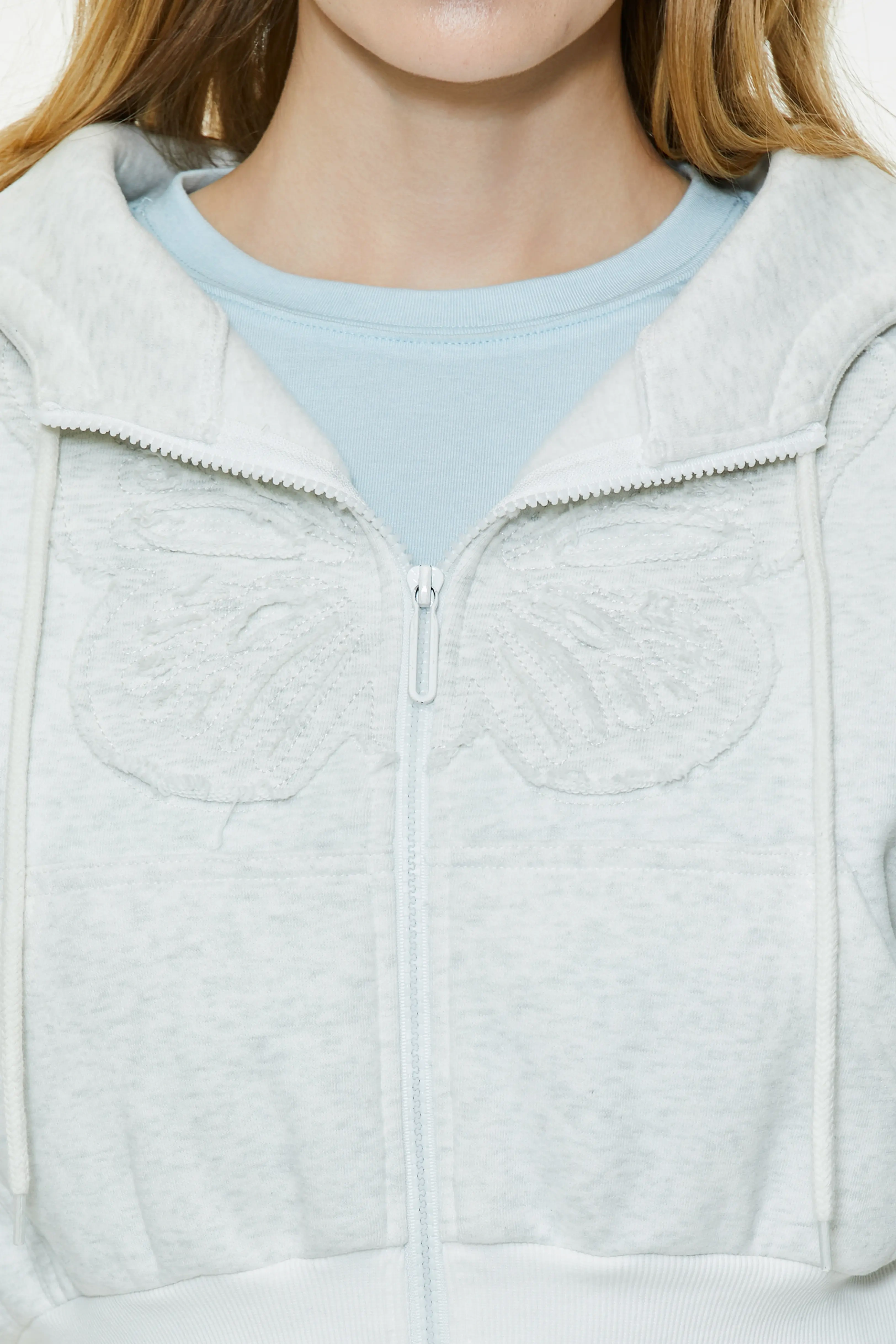 Close-up shot showing the full zip closure, spread collar design, and subtle butterfly pocket outline of the heather grey hoodie.