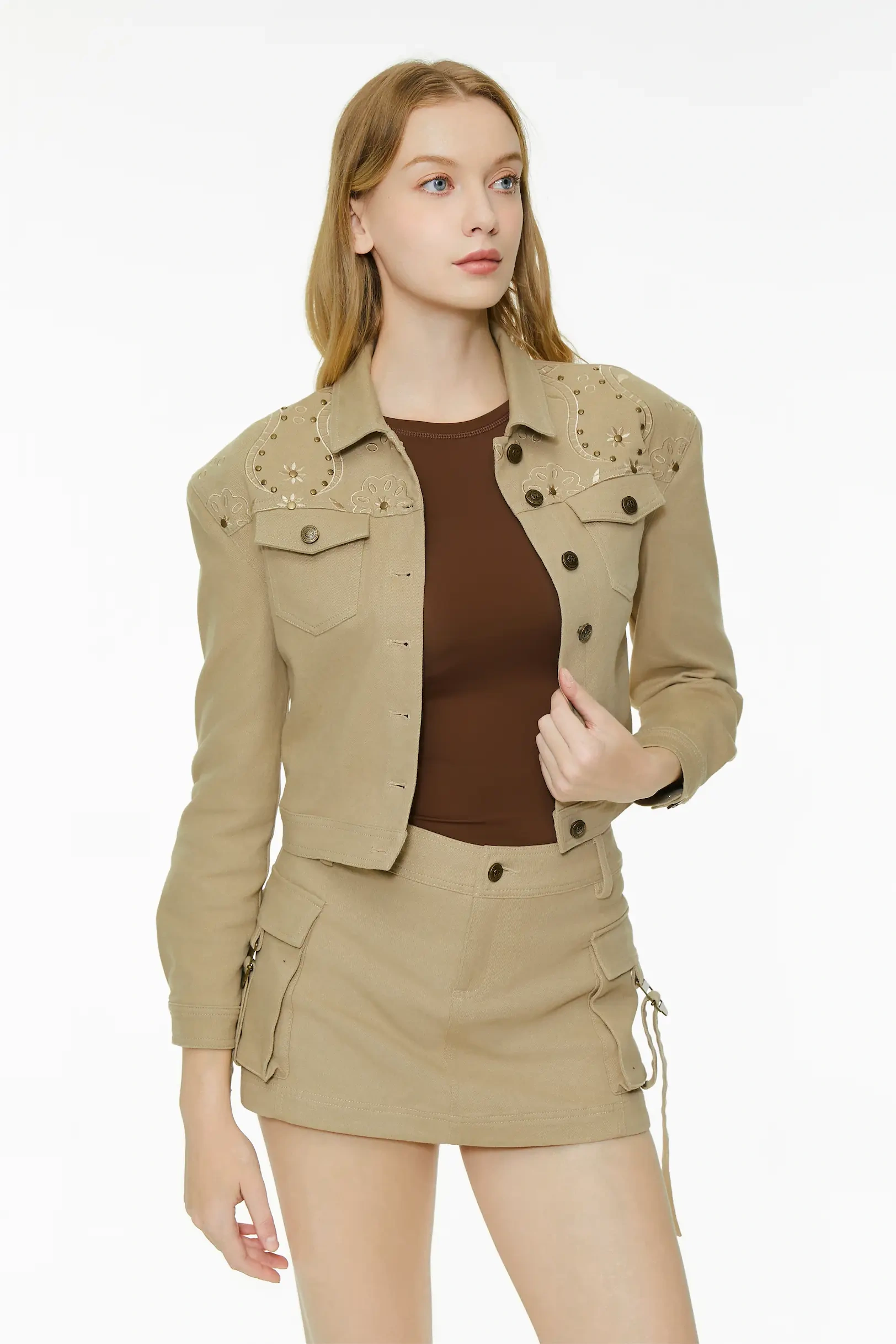 Three-quarter full body view of a model wearing a khaki studded cropped jacket and high-waisted cargo skirt set.