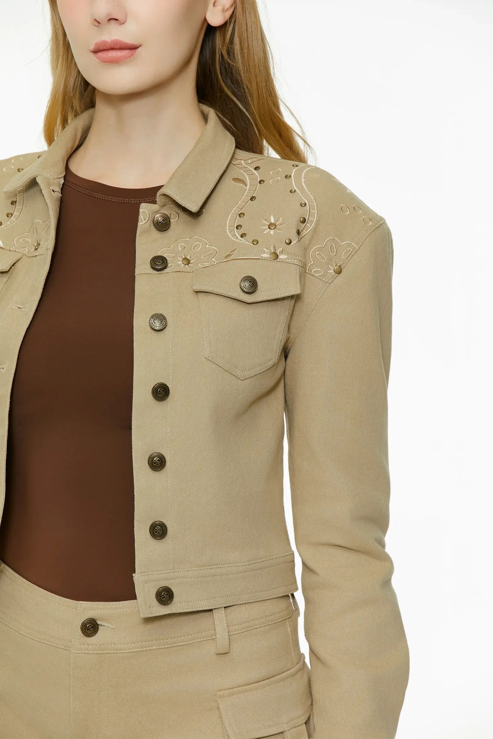 Upper body close-up shot showcasing the point collar, metallic studs, front button placket, and chest pocket on the khaki cropped jacket.